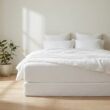Frisch bezogenes Bett mit weißer Matratze im hellen Schlafzimmer